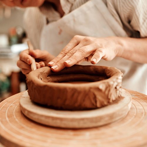 Hands, clay and pottery wheel in studio with tools, craft and skills for product at small business. Person, artist and entrepreneur with material, creativity and manufacturing at startup factory.